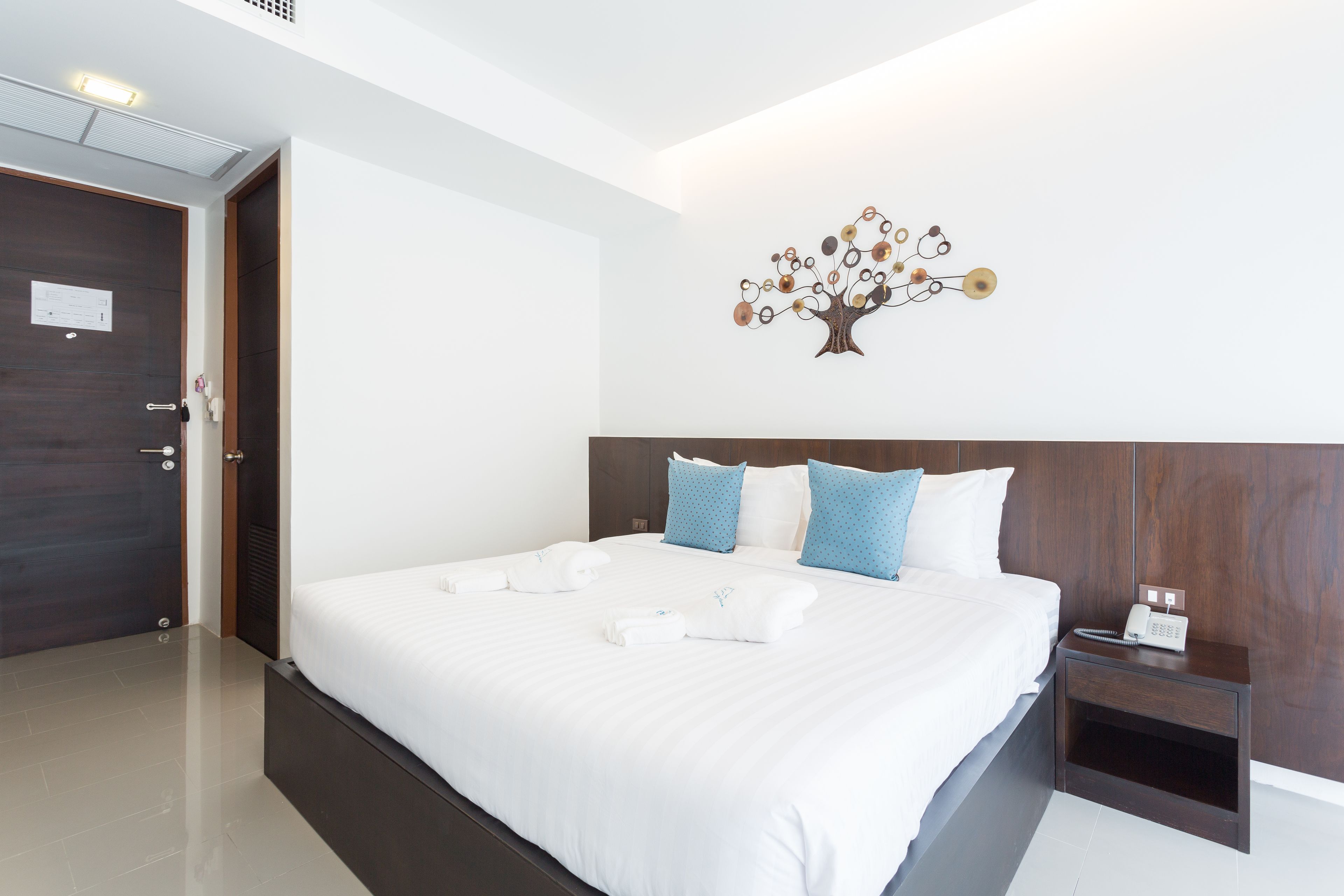 A hotel room with a large bed, a wooden headboard, a nightstand with a phone, and a wall art piece.
