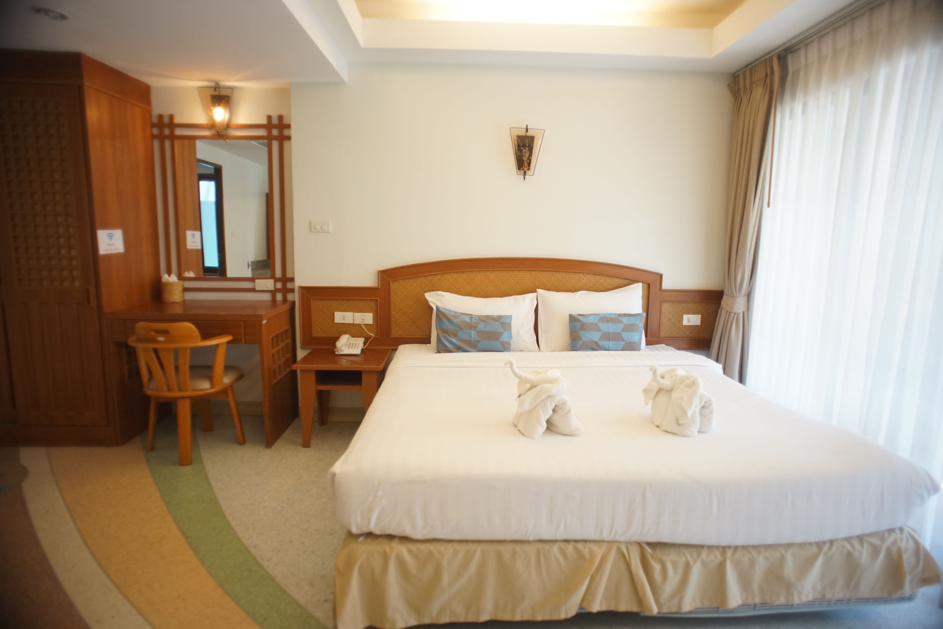 A hotel room with a large bed, a desk, a chair, and a mirror.