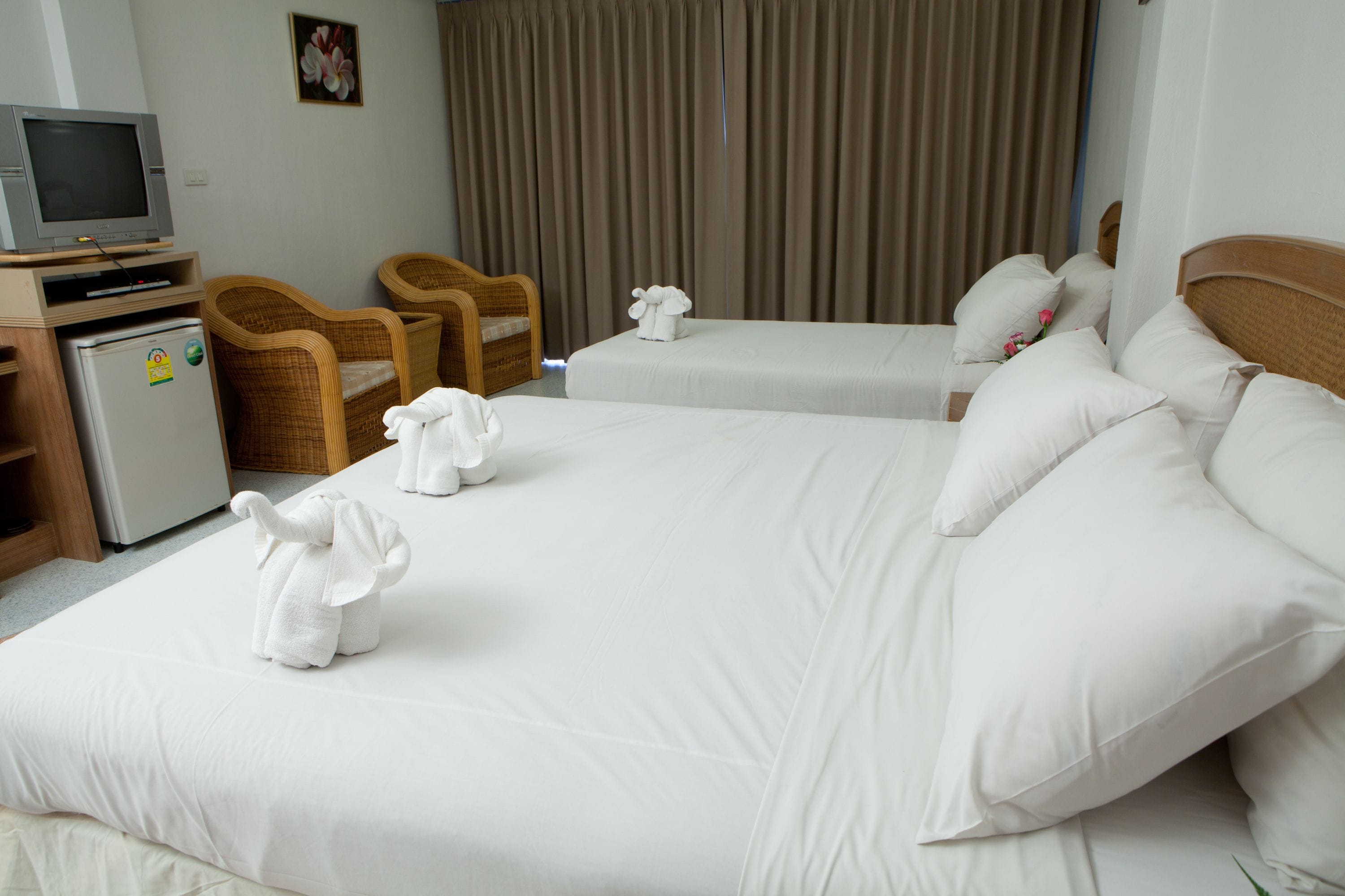 A hotel room with two beds, a television, a refrigerator, and wicker chairs.