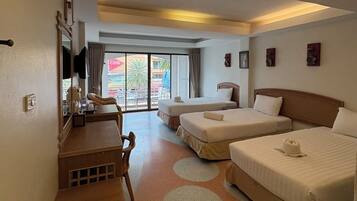 Quarto de hotel com duas camas, uma escrivaninha e uma cadeira. Há uma janela grande com vista para palmeiras e um edifício.