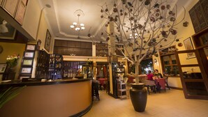 A restaurant with a central tree sculpture, a bar area, and a seating section with tables and chairs. - Anise Hotel & Restaurant (Phnom Penh)