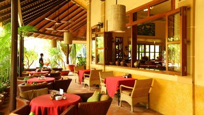 An outdoor restaurant with wicker furniture, red tablecloths, and a tiled floor. - Anise Hotel & Restaurant (Phnom Penh)