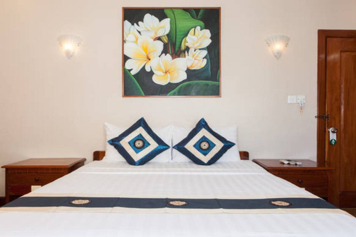 A hotel room with a bed, two nightstands, a wooden door, and a wall-mounted painting of flowers.
