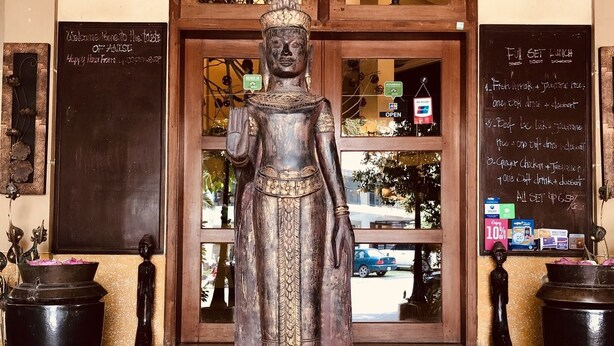 A Buddha statue in front of a building with a signboard and a flower arrangement. - Anise Hotel & Restaurant (Phnom Penh)