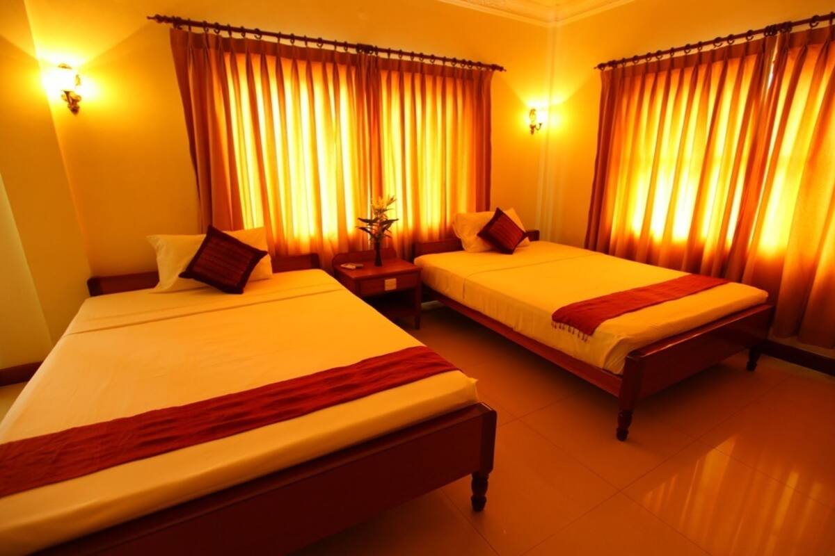 A hotel room with two beds, each with a red throw blanket, a nightstand, and a vase with flowers.