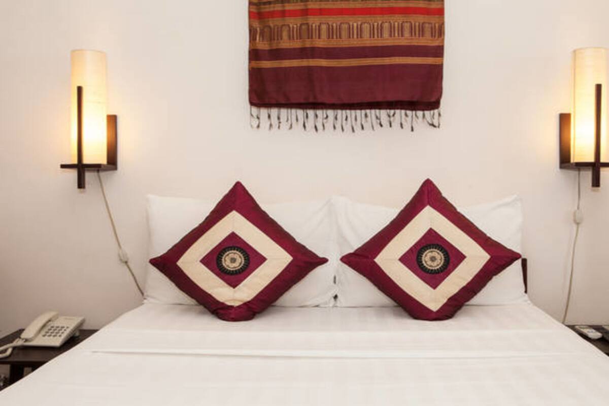 A hotel room with a bed, two decorative pillows, a wall hanging, and two wall-mounted lamps.