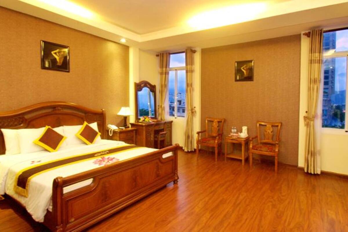 Une chambre d’hôtel avec un grand lit, deux fauteuils, un bureau et une fenêtre donnant sur la ville.