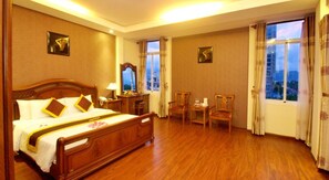 Une chambre d’hôtel avec un grand lit, deux fauteuils, un bureau et une fenêtre donnant sur la ville.