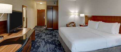 A hotel room with a large bed, a desk with a television, a chair, and a lamp.