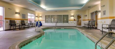 An indoor swimming pool with a tiled floor, a pool ladder, and several chairs around the pool area.