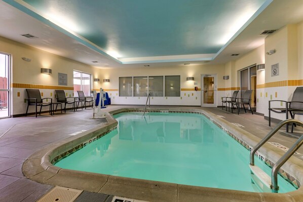 Una piscina interior con suelo de baldosas, una escalera de piscina y varias sillas alrededor del área de la piscina.