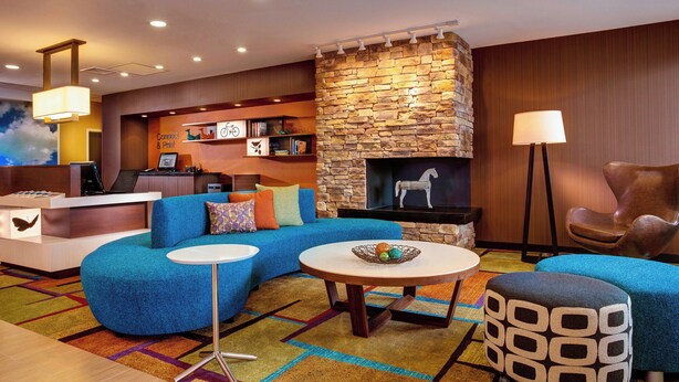 Een moderne hotel lobby met een stenen openhaard, een blauwe bank, een ronde tafel en een klein pouf.