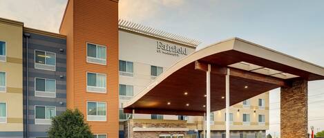 Een meerlaags hotel met een opvallend Fairfield by Marriott bord, een overdekte ingang en een parkeerplaats met auto's.