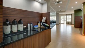 Een receptiezone met een houten balie, waterdispensers, een koffieapparaat en een schaal met snacks.