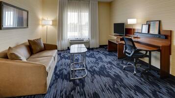Une chambre d’hôtel avec un canapé, un bureau avec une chaise, une télévision et une lampe.