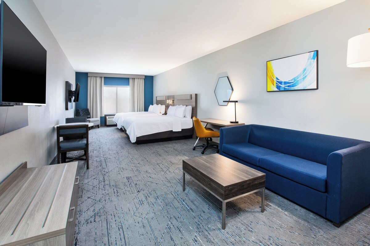 Una habitación de hotel con una cama, un sofá azul, un escritorio, un televisor y un cuadro en la pared.