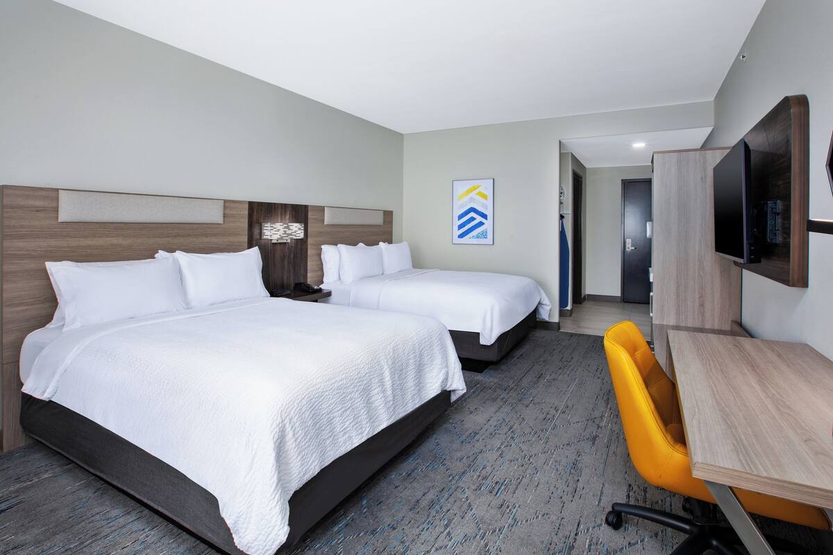 A hotel room with two beds, a desk, and a chair.