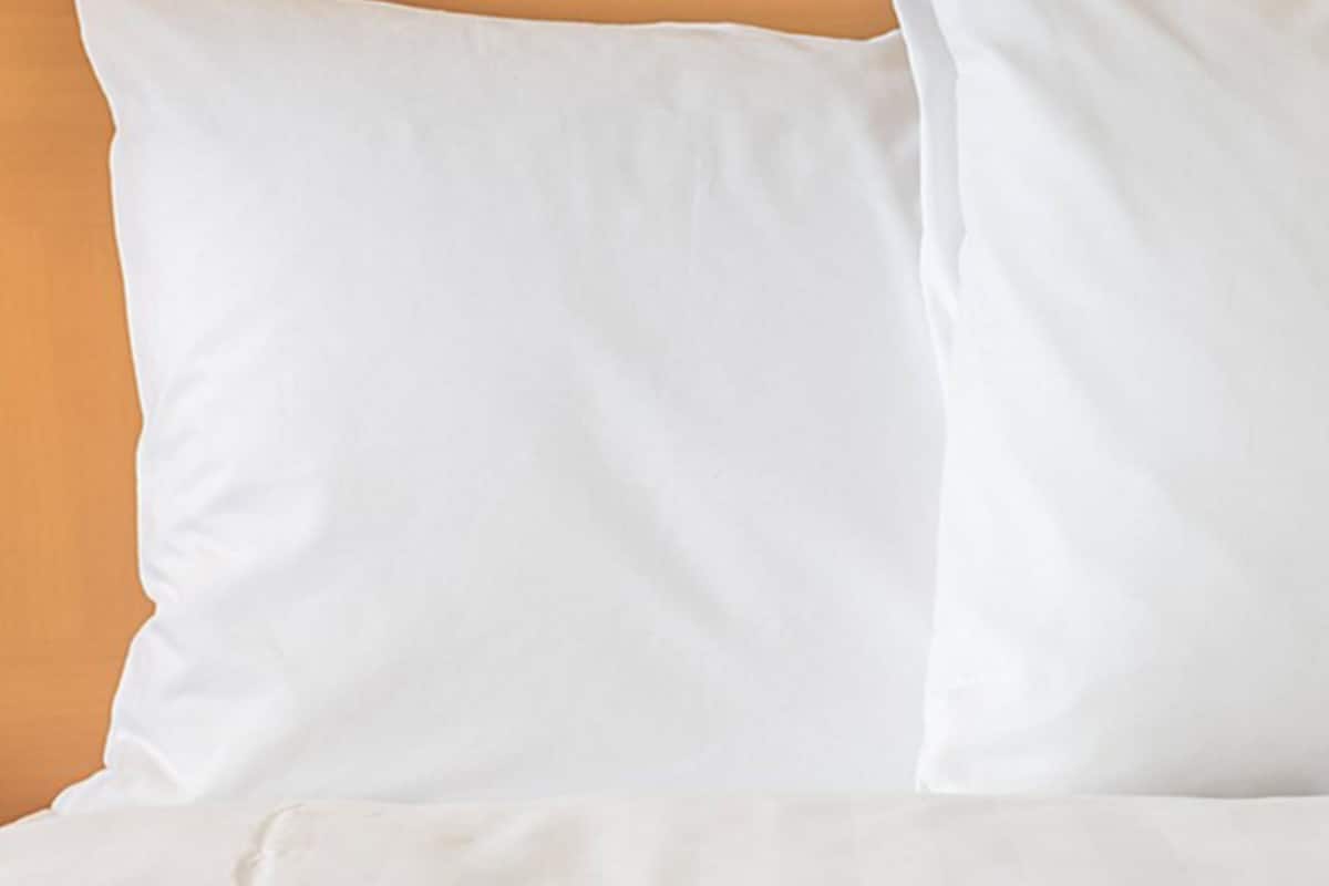 A close-up of a white pillow against a beige wall.