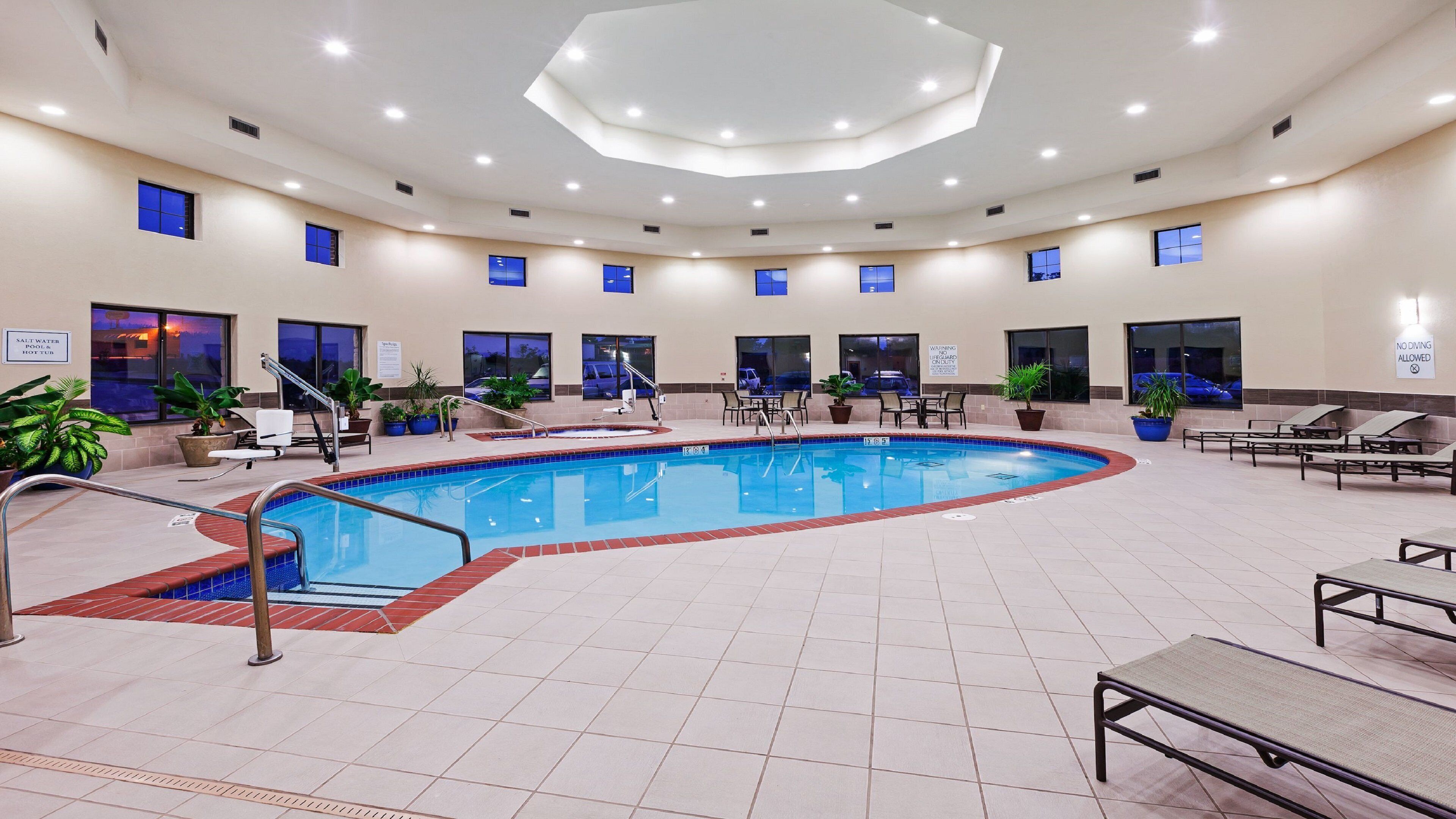 A hotel pool area with a large pool, sun loungers, and a staircase leading to an upper level.