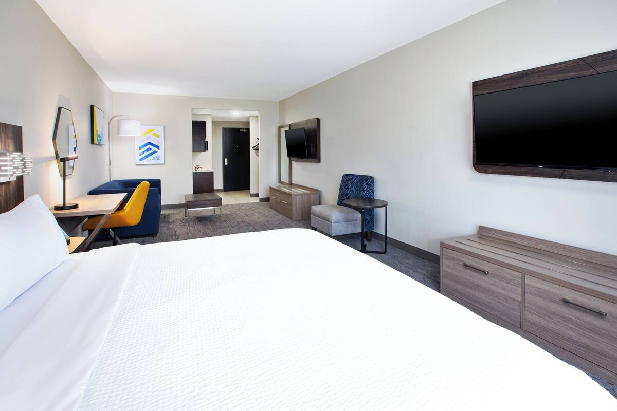A modern hotel room with a large bed, a desk, a chair, a TV, and a wardrobe.