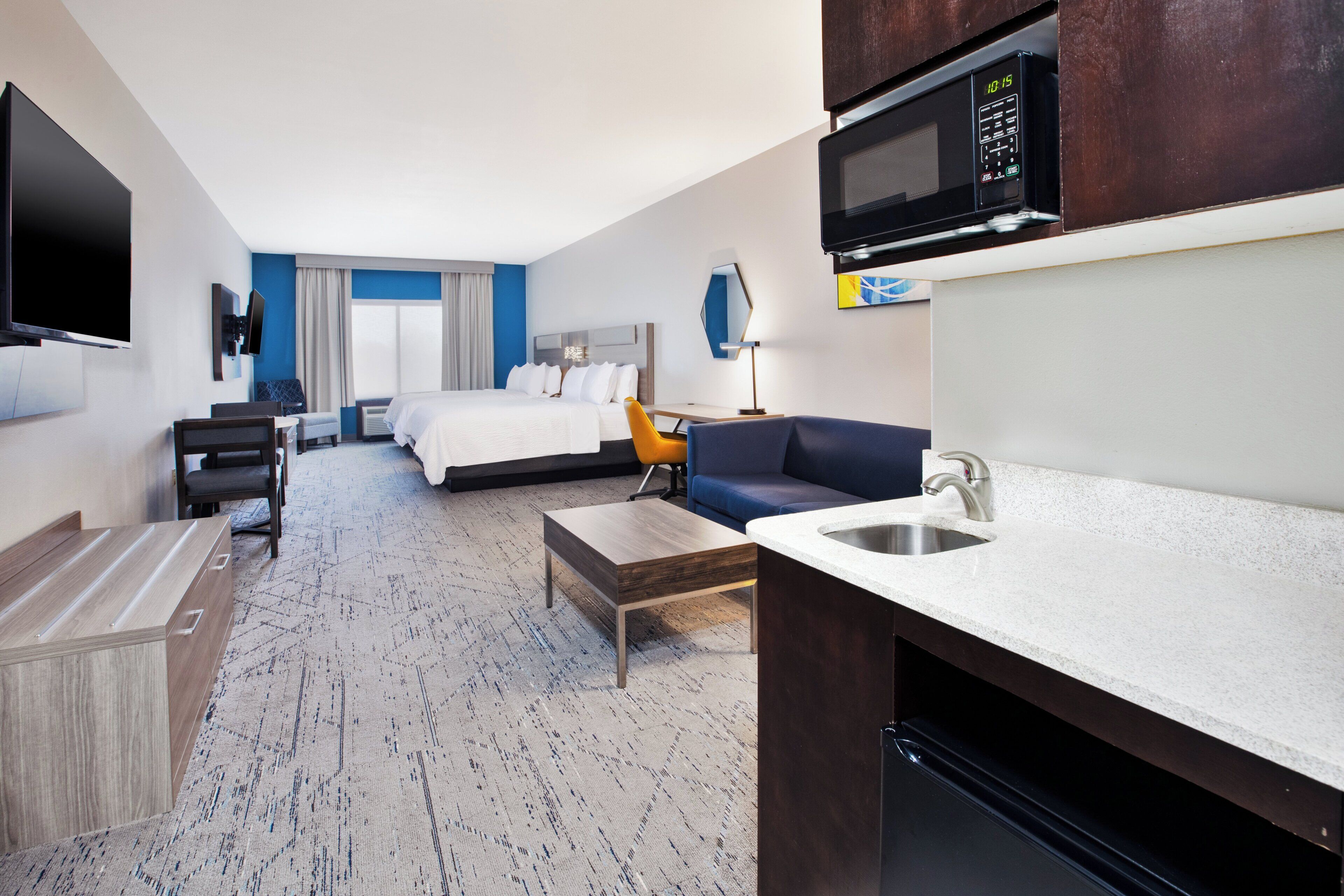 Habitación de hotel con cama, escritorio, silla, sofá, televisor, microondas y lavabo.