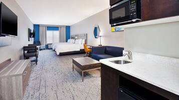 Habitación de hotel con cama, escritorio, silla, sofá, televisor, microondas y lavabo.