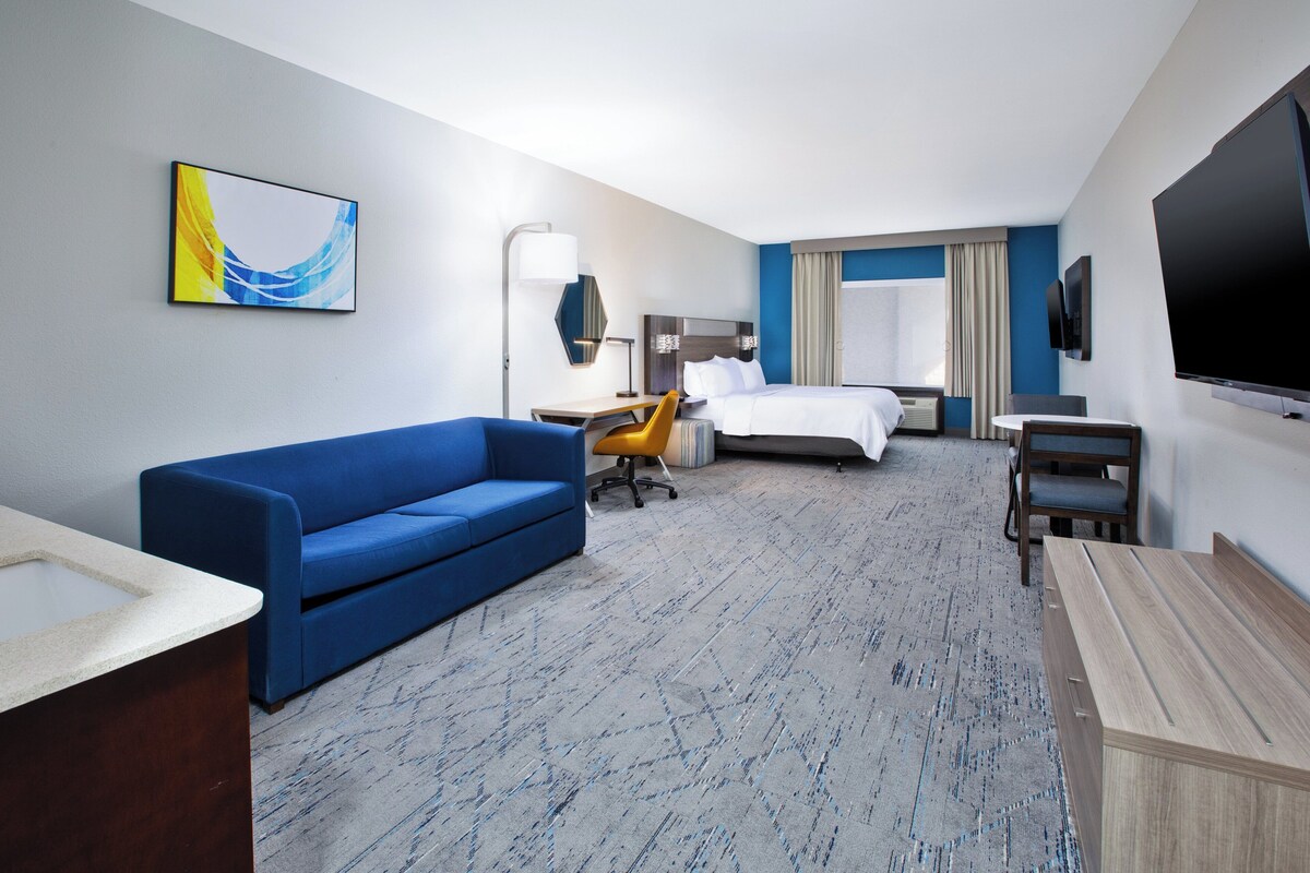 Habitación de hotel con sofá azul, cama, escritorio, silla y televisor.
