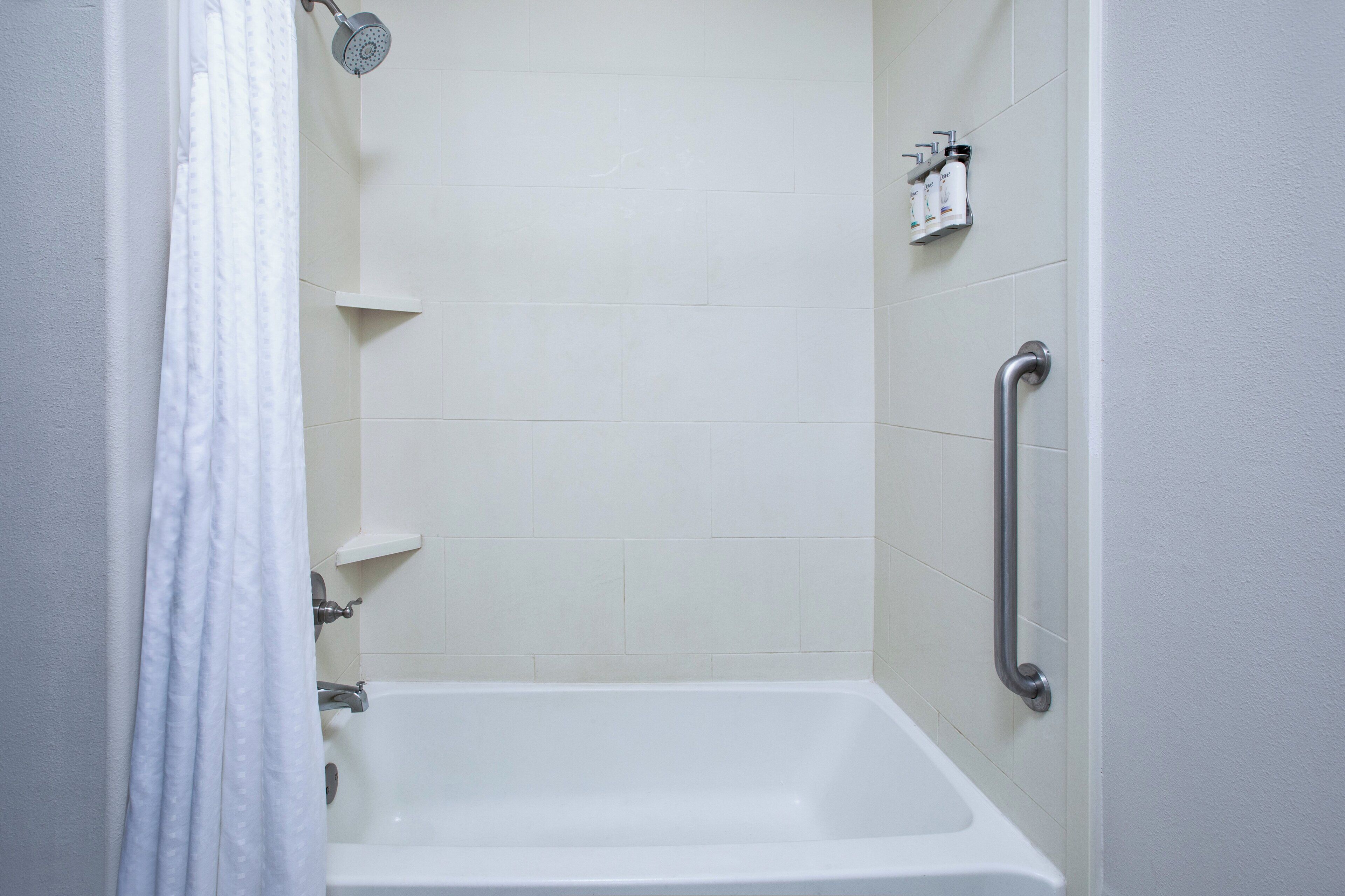 A bathroom with a white bathtub, a showerhead, and a handrail.