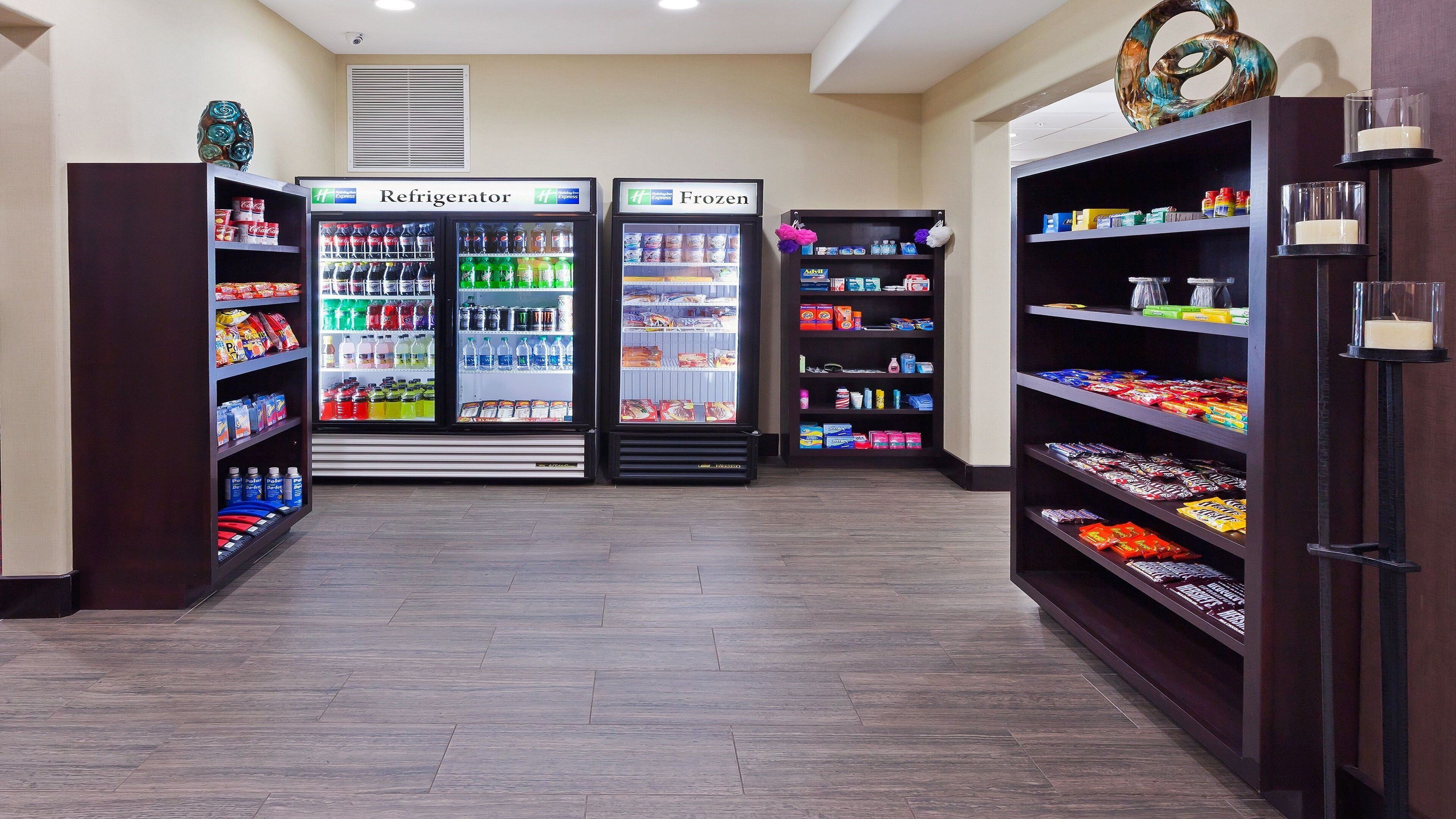 A hotel lobby with a refrigerator and frozen food display, shelves with snacks, and a decorative item on the wall.