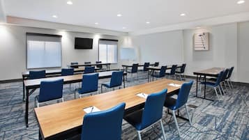 Une salle de conférence avec une longue table, des chaises bleues, un tableau blanc et un téléviseur à écran plat fixé au mur.