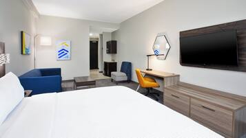 A hotel room with a large bed, a desk with a chair, a TV mounted on the wall, and artwork on the walls.