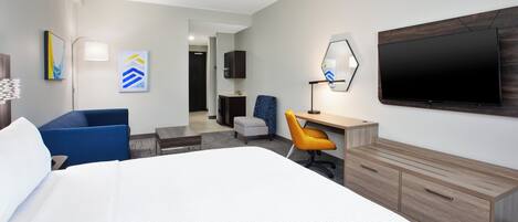 A hotel room with a large bed, a desk with a chair, a TV mounted on the wall, and artwork on the walls.