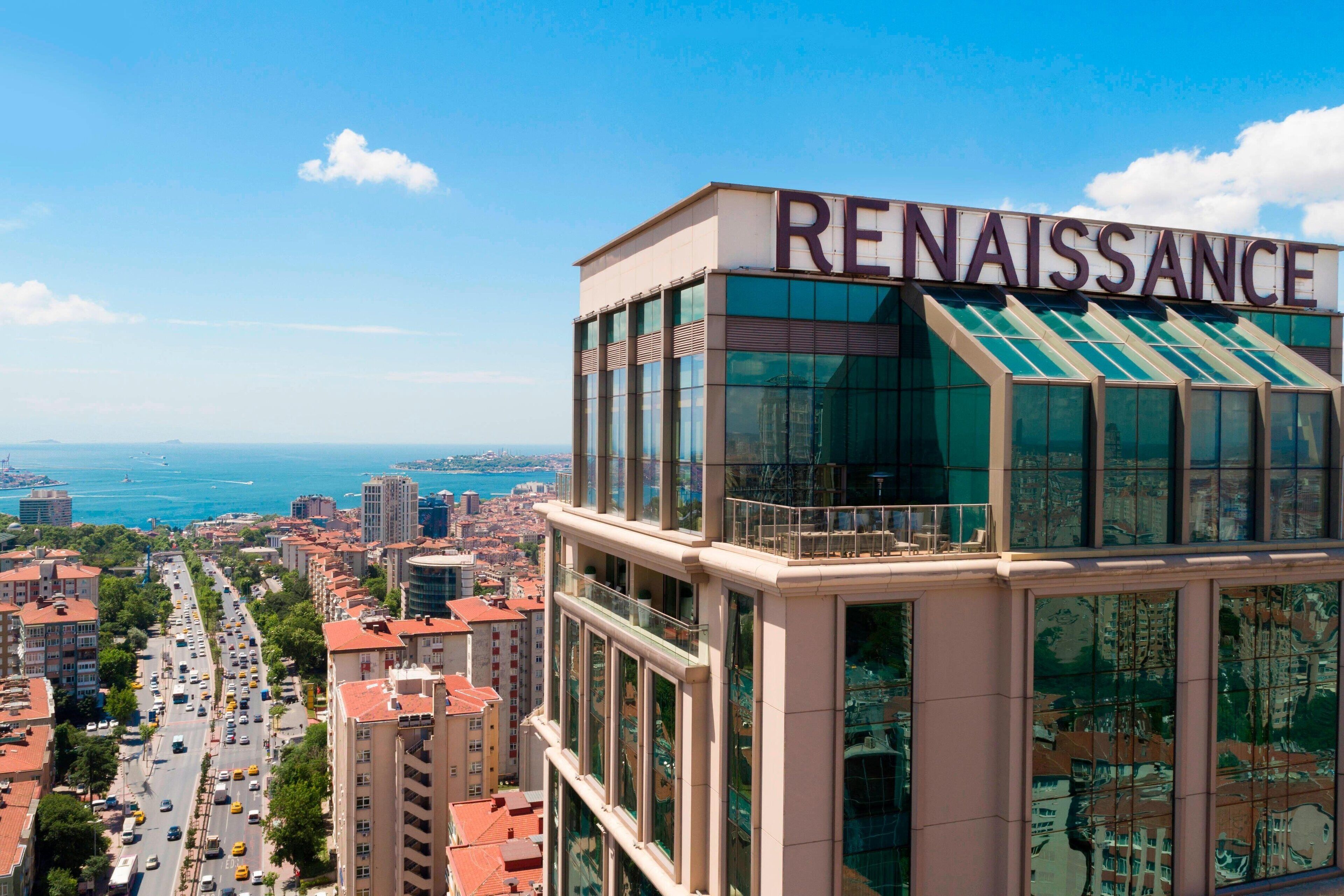 A modern building with the sign "RENAISSANCE" on top, featuring large windows and a view of the city and sea.