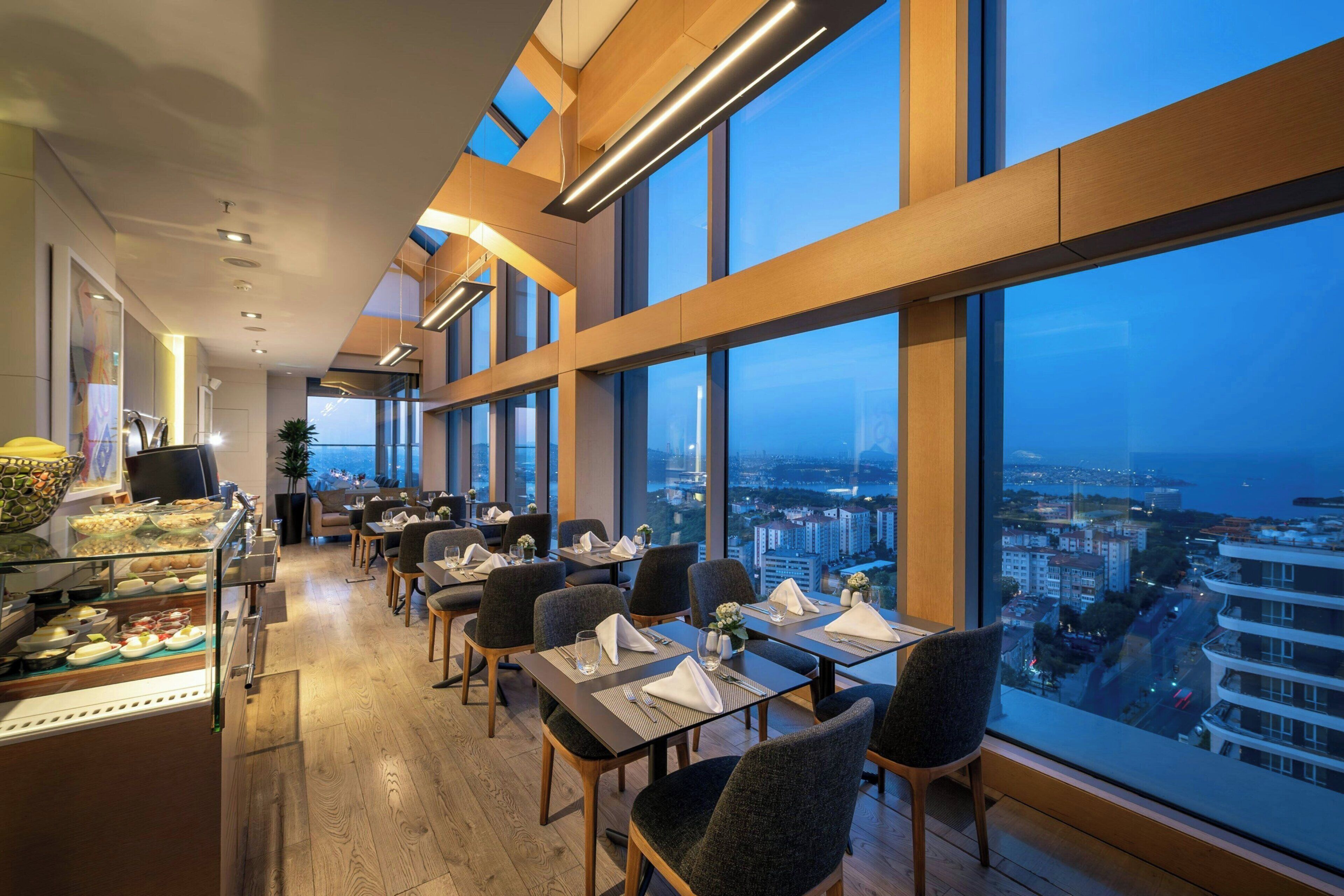 A restaurant with tables set for dining, large windows, and a city view.