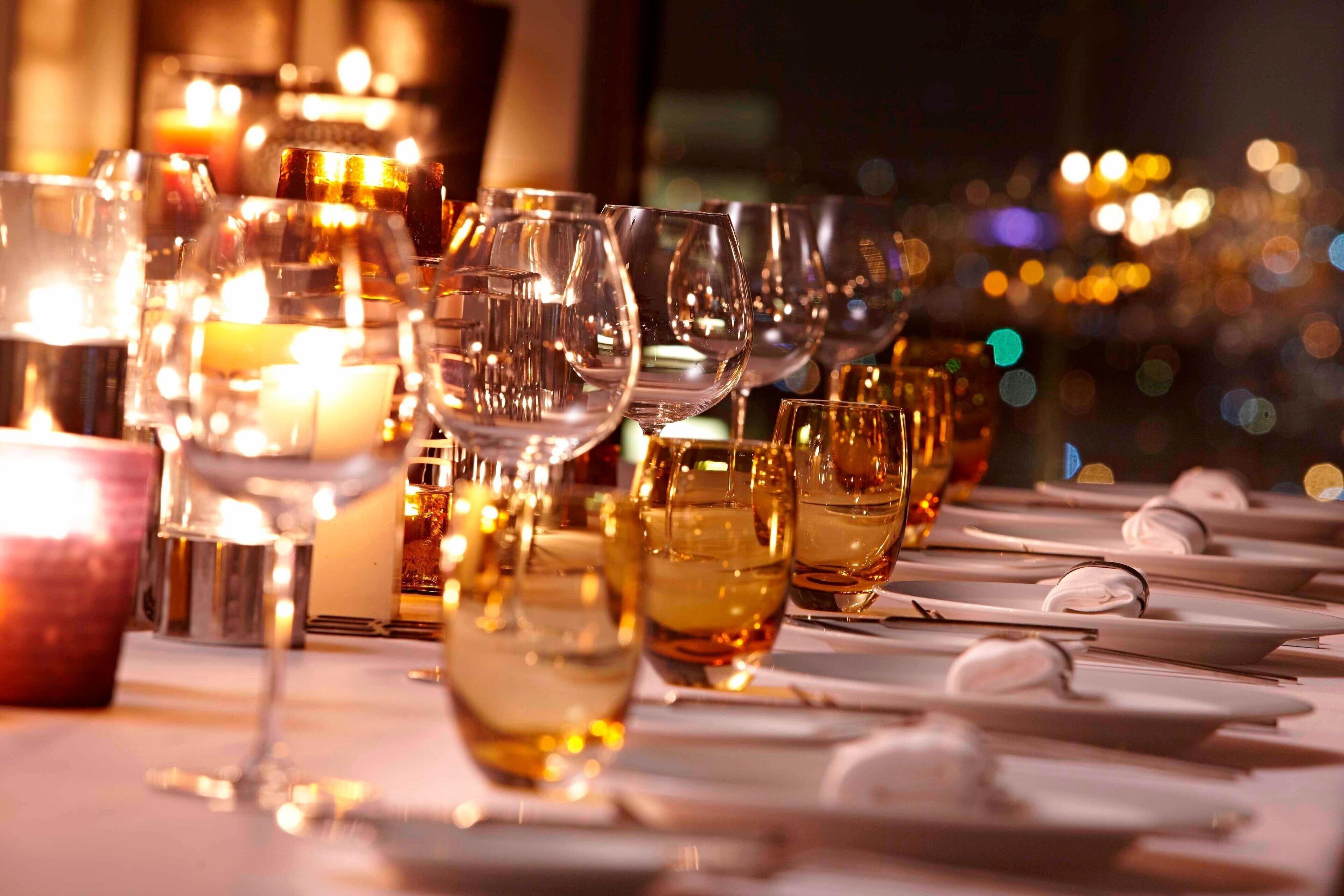A table set with multiple wine glasses and plates, candles, and a warm ambient light.