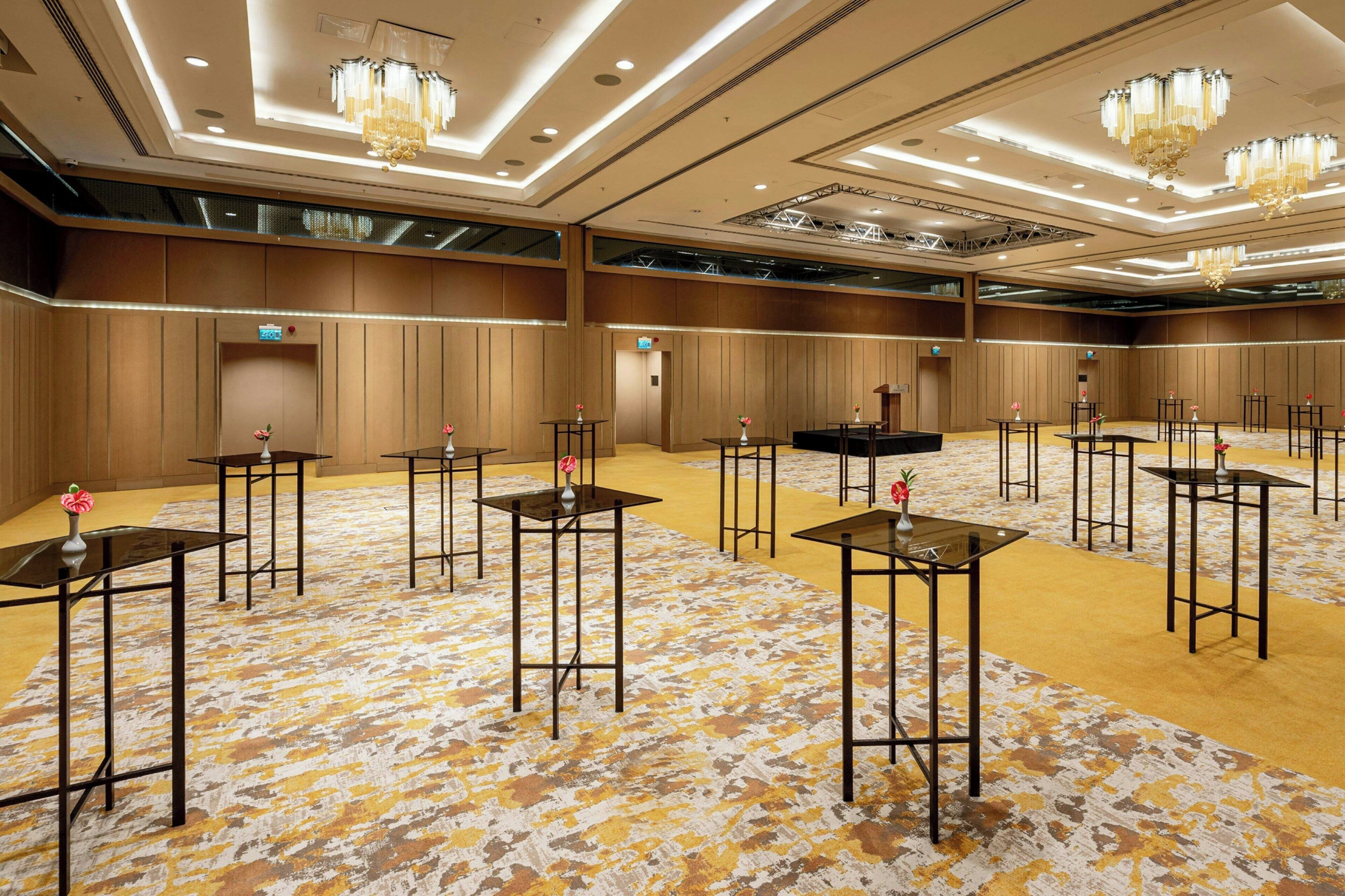 A large conference room with multiple tables and chairs, a patterned carpet, and chandeliers.