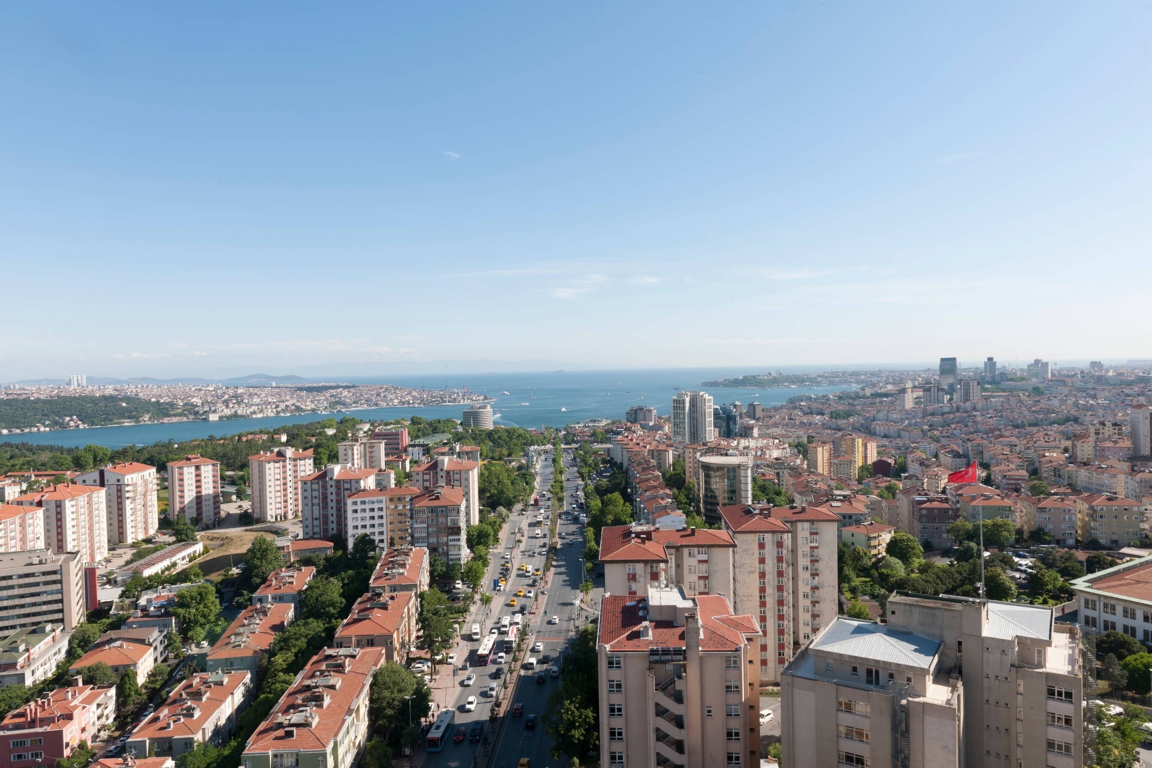 A cityscape with high-rise buildings, a central road, and a body of water in the distance.