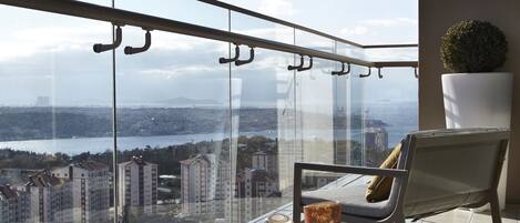 A balcony with a glass railing, a table with a cushion, and a potted plant.