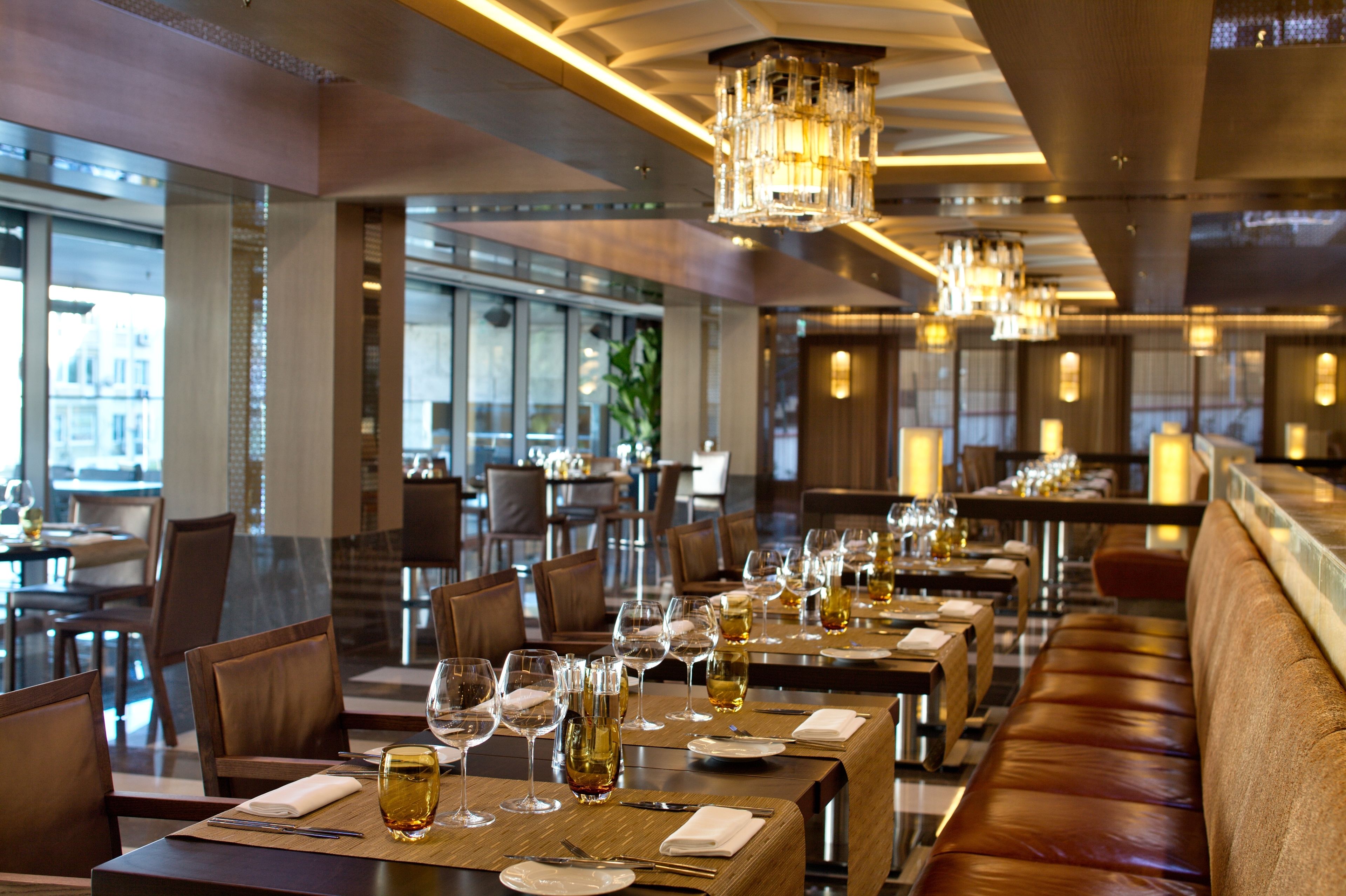 Restaurante com mesas compridas preparadas para refeições, com interior moderno, mobiliário de madeira e iluminação ambiente.
