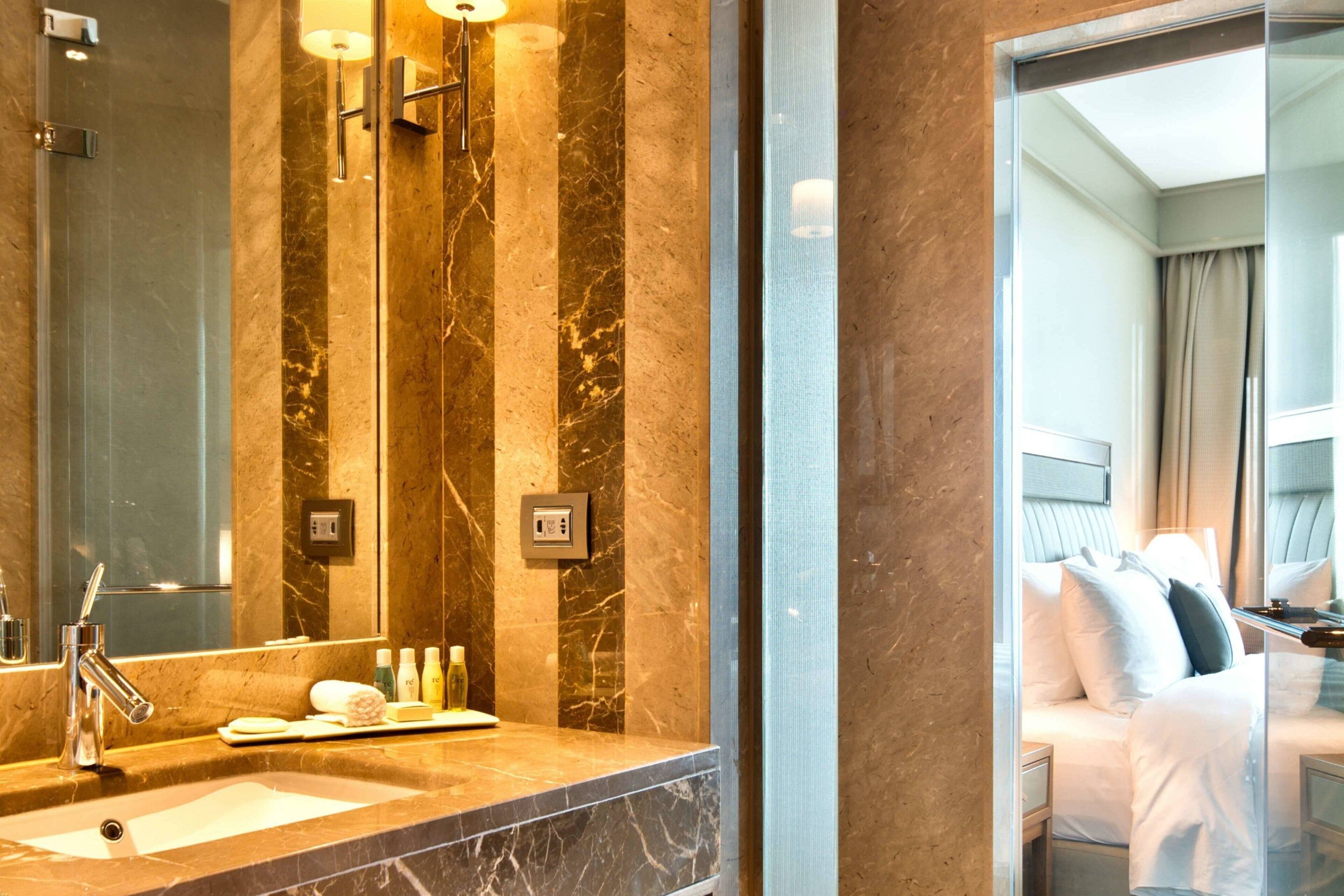 A modern bathroom with a marble countertop, a large mirror, and a glass shower enclosure.