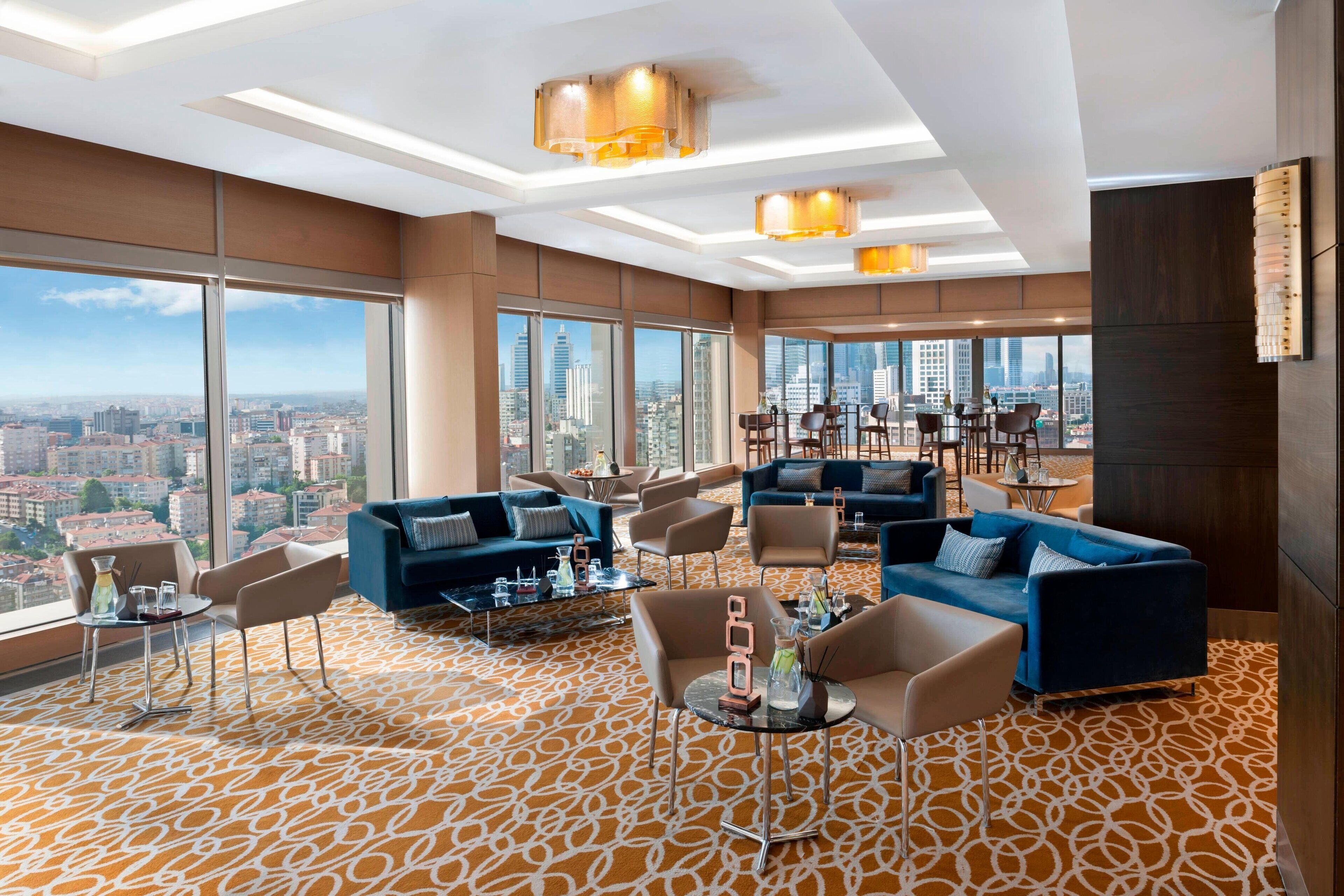 A modern hotel lobby with large windows, comfortable seating, and a city view.