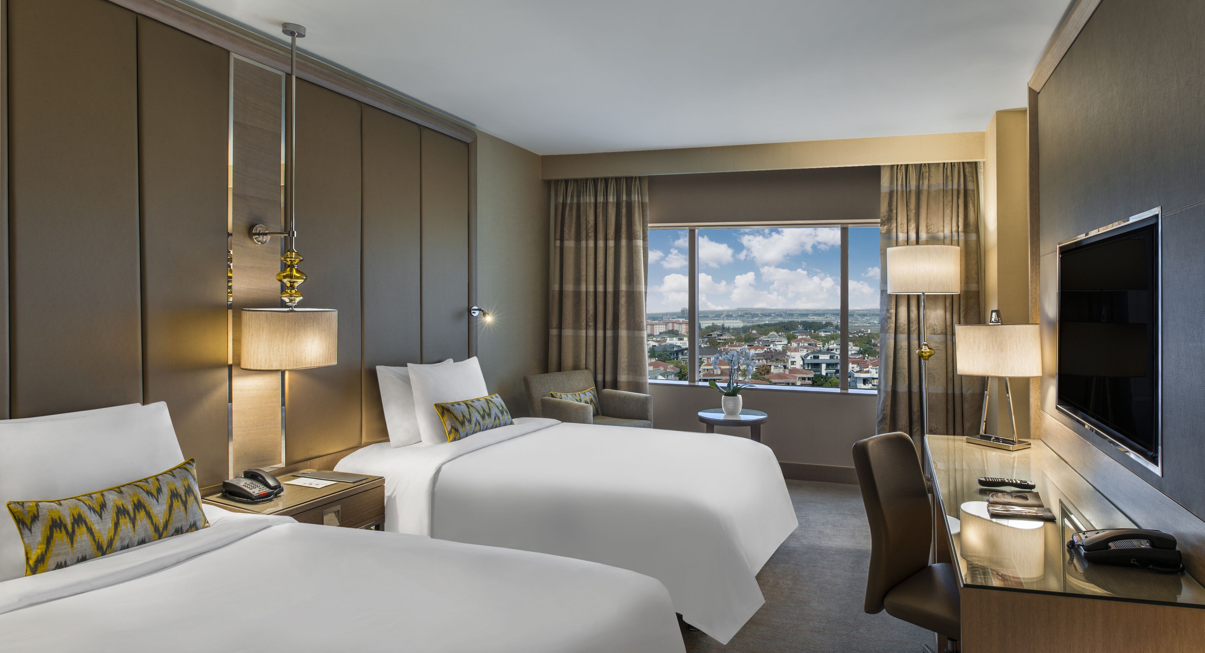 Habitación de hotel con dos camas, un escritorio, un televisor y vista a la ciudad.