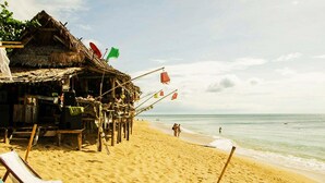Uma praia com uma cabana de telhado de palha, areia dourada e céu claro.