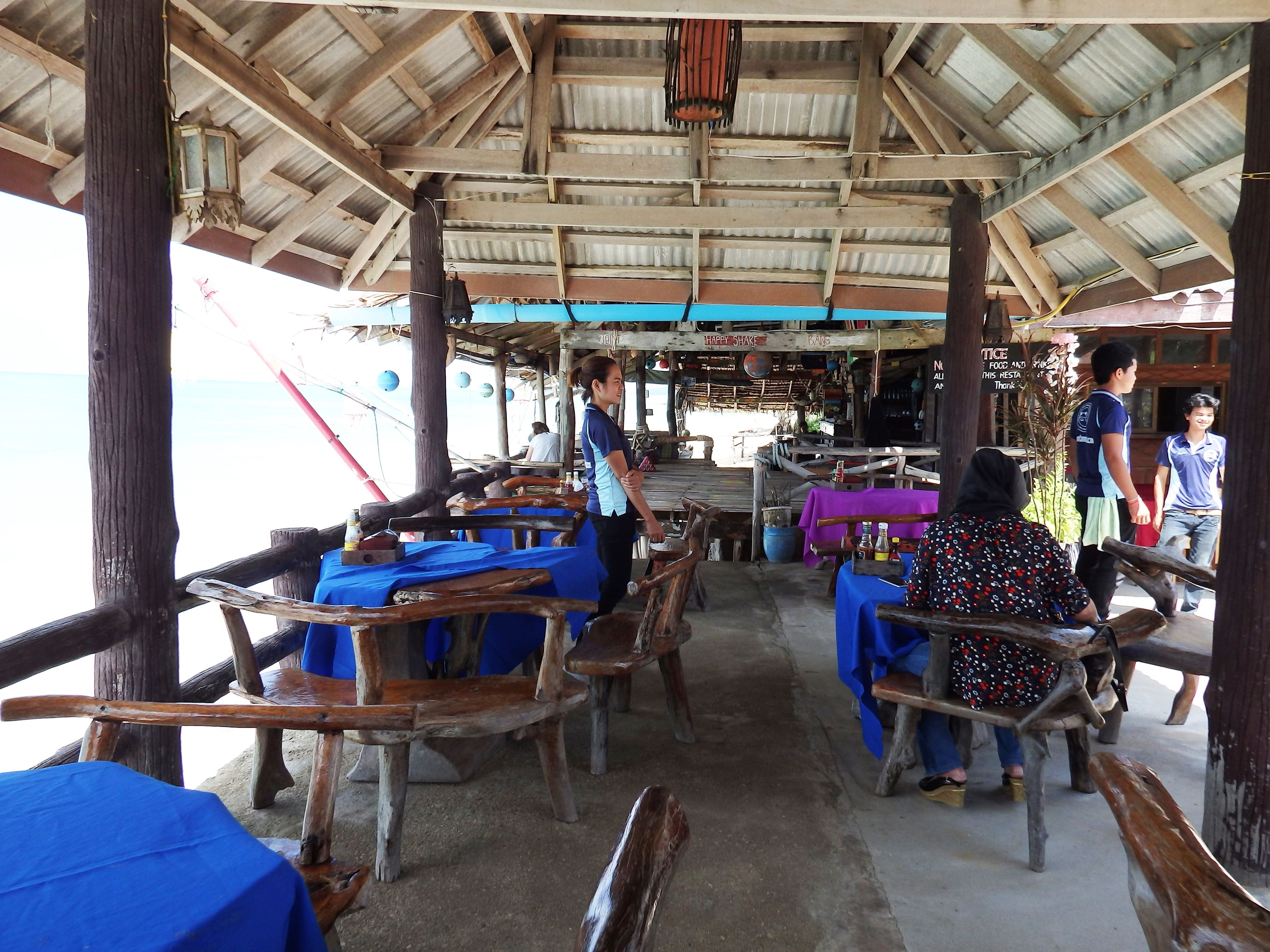A rustic wooden structure with tables and benches, a blue tablecloth, and a sign that reads "HAPPY SHAKE".