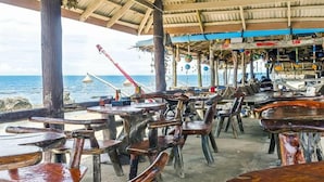 Um restaurante à beira-mar com mesas e cadeiras de madeira, com vista para o oceano.