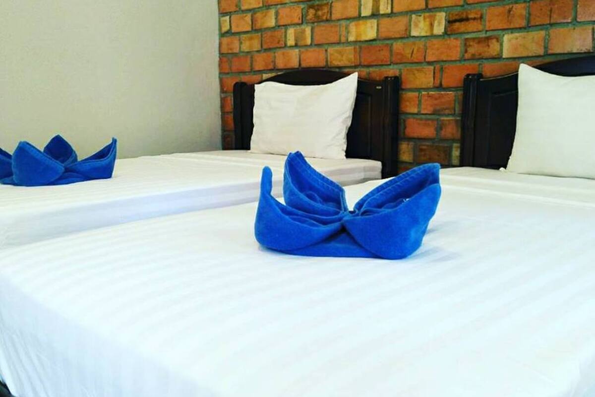 Une chambre d’hôtel avec deux lits, chacun recouvert d’une courtepointe blanche et agrémenté de serviettes bleues.