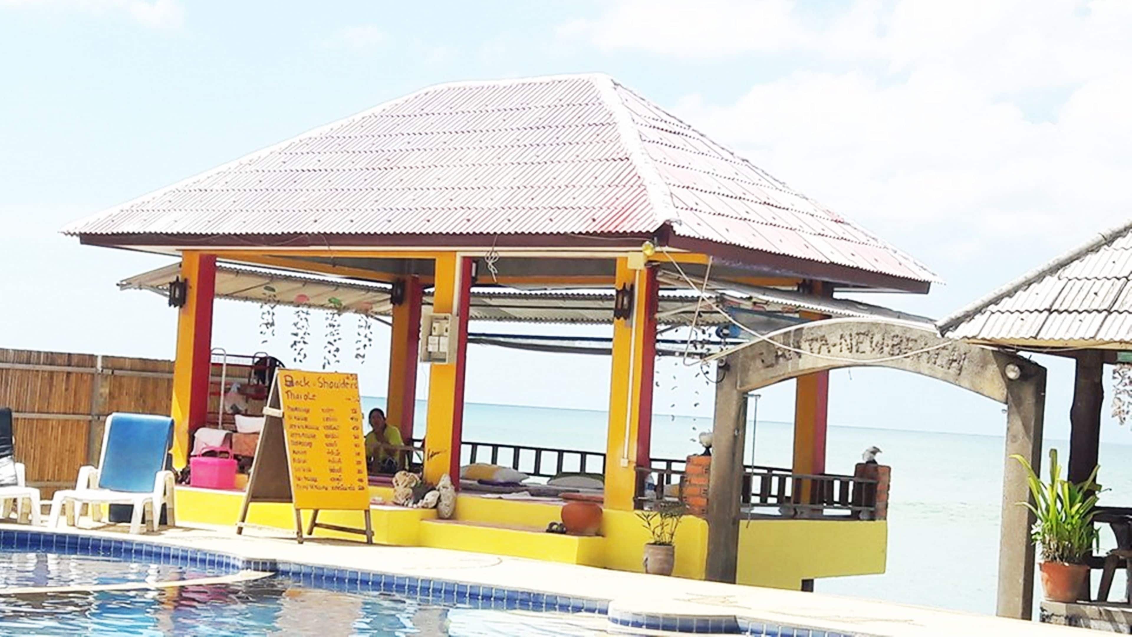A poolside area with a covered seating area, a signboard, and a view of the sea.