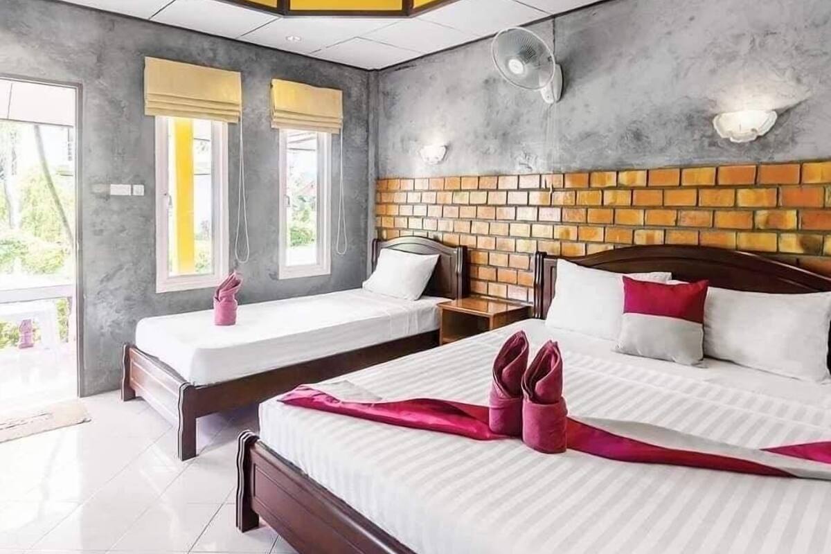 Une chambre d’hôtel avec deux lits, un mur décoratif en briques, une grande fenêtre avec stores et un ventilateur de plafond.