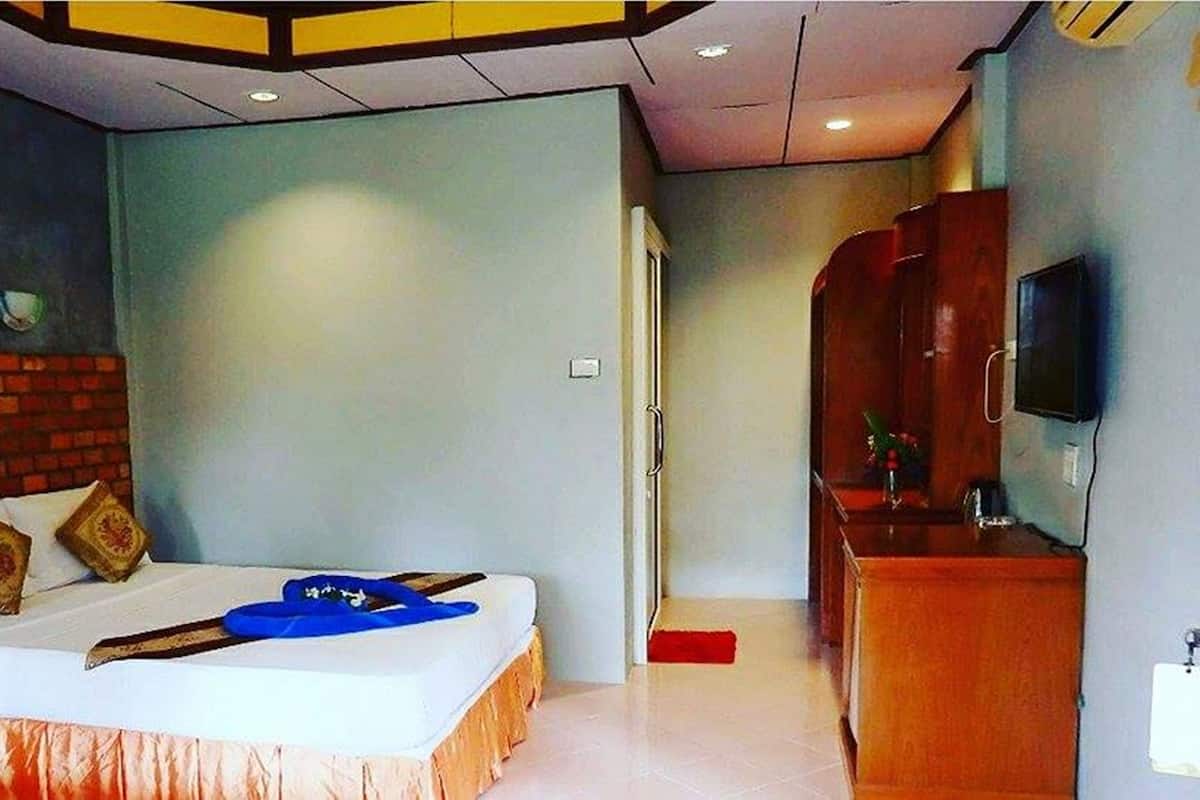 Une chambre à coucher avec un lit, une commode en bois, un téléviseur et un mur décoratif en briques.