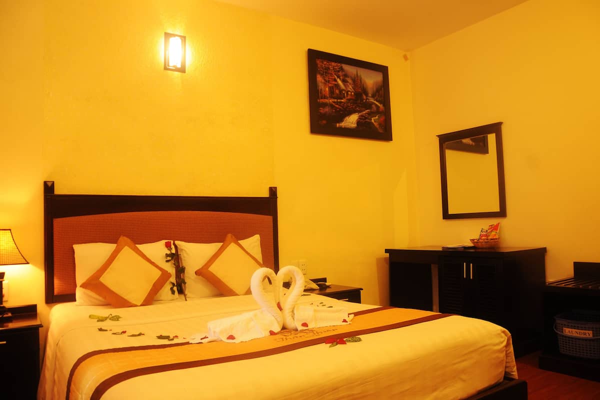 Habitación de hotel con cama, mesita de noche, lámpara, un cuadro en la pared y un espejo.